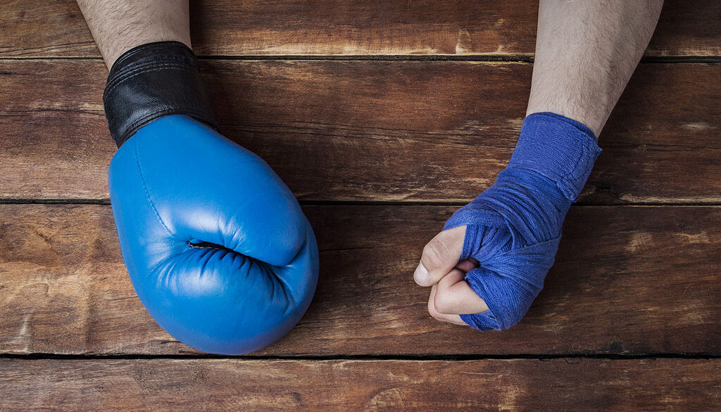 Closeup Of A Man’s Hand In A Boxing Glove And The Other Covered In Hand Wrap Sitting On A Wooden Table What Is A Boxer’s Fracture