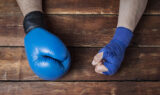 Closeup Of A Man’s Hand In A Boxing Glove And The Other Covered In Hand Wrap Sitting On A Wooden Table What Is A Boxer’s Fracture