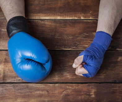 Closeup Of A Man’s Hand In A Boxing Glove And The Other Covered In Hand Wrap Sitting On A Wooden Table What Is A Boxer’s Fracture