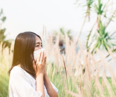 An Asian Woman Standing Amongst Weeds Covering Her Nose Dealing with Ragweed Allergy Symptoms.