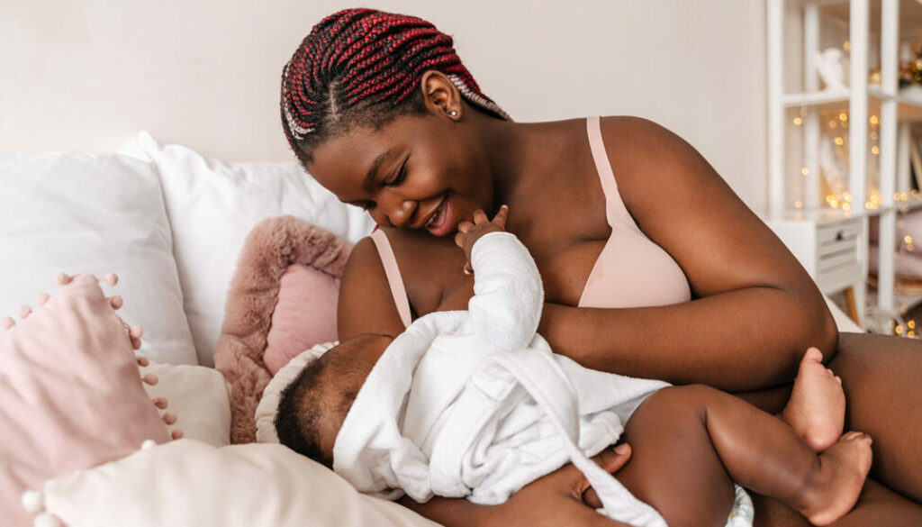 Young african american woman breastfeeding her baby in bedroom