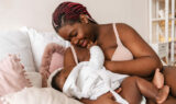 Young african american woman breastfeeding her baby in bedroom