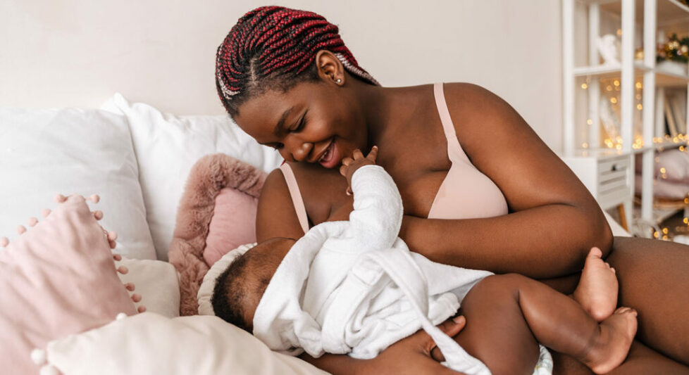 Young african american woman breastfeeding her baby in bedroom