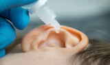 Closeup of a Doctor Wearing Blue Gloves Dripping Ear Drops Into a Patient’s Ear Can Earwax Cause Tinnitus